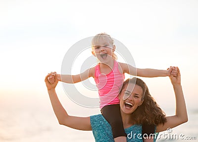 Baby girl sitting on shoulders of mother on beach Stock Photo