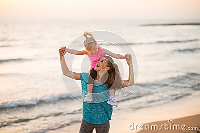 Baby girl sitting on shoulders of mother on beach Stock Photo