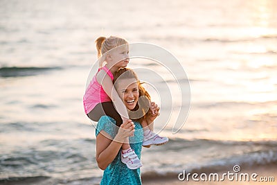 Baby girl sitting on shoulders of mother on beach Stock Photo