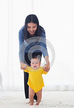 Baby girl taking first steps learning to walk with mom Stock Photo