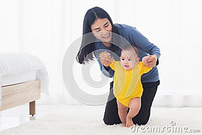Baby girl taking first steps learning to walk with mom Stock Photo