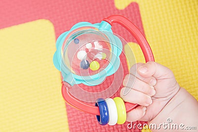 Baby hand holding a rattle on a colored rubber mat puzzle for playing foam with geometric figures Stock Photo