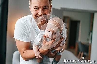With baby in hands. Smiling, having fun. Father with toddler is at home, taking care of his son Stock Photo