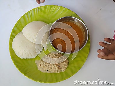 Baby Holding in Hand Home Made Indian vegetarian rice cakes breakfast known as idli or idly, served with sambar and Chatney in a Stock Photo