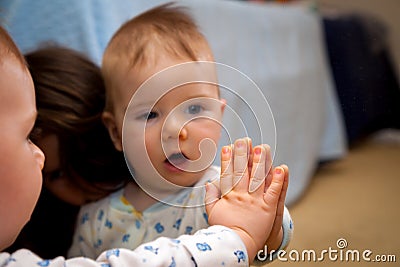 Baby Holds His Hand On A Mirror and Is Amazed By The Reflection Stock Photo