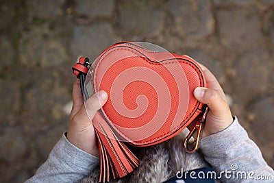 Baby holds a small heart shaped red bag. Grey background. Accessories and love contest. Little lady. Saint Valentines Stock Photo