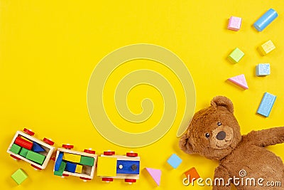 Baby kids toys background with teddy bear, wooden train, colorful blocks and bricks on yellow background. Top view Stock Photo