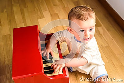 Baby learning to play the piano with a wooden toy instrument, a tender and funny childhood scene Stock Photo