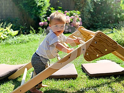 Baby learning to stand and climb on a wooden triangle Stock Photo