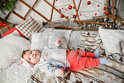 Baby lies on red and white christmas background. Photo of a healthy, chubby baby lying on its back, playing with toes, wearing a Stock Photo