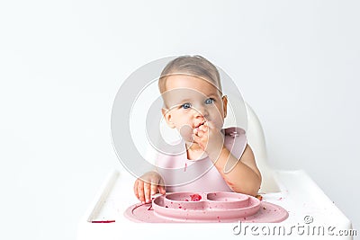 baby little sits in a high chair and eats complementary foods. , close-up portrait looks at the camera. baby food concept Stock Photo