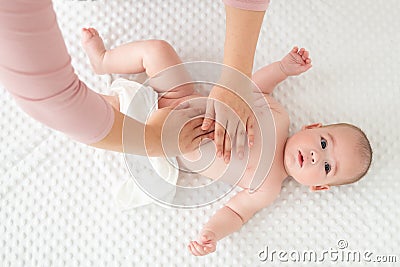 Baby massage. Female therapist gently massaging newborn baby boy. Mother applying body lotion to her infant baby boy. Stock Photo