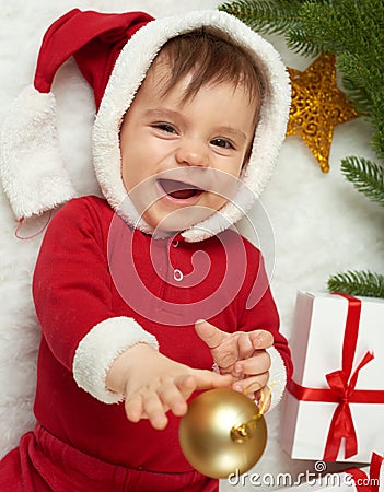 Baby portrait in christmas decoration, dressed as Santa, lie on fur near fir tree and play with gifts, winter holiday concept Stock Photo