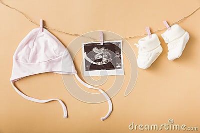 baby s cap ultrasound picture pair woolen shoes hanging clothesline against orange backdrop. High quality photo Stock Photo