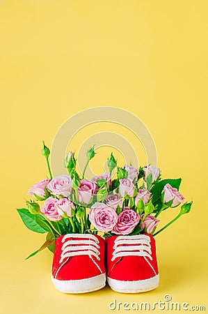 Baby shoes filled with rose flowers on yellow background Stock Photo