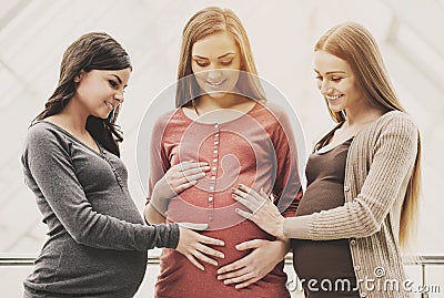 Baby shower. Two cheerful women are touching their pregnant friend belly Stock Photo