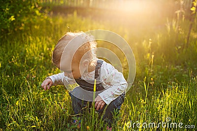 Baby sitting in the grass in sunlight. Cute summer blond girl in the garden Stock Photo