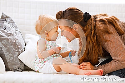 Baby with soother and young mom playing on divan Stock Photo