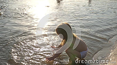 Baby splashing in the water. splashing water. Cute child happily plays on the beach. happy child bathes in the sunset on Stock Photo