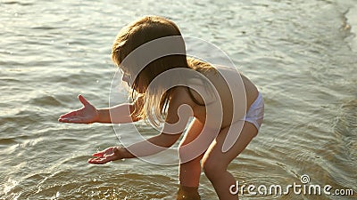 Baby splashing in the water. splashing water. Cute child happily plays on the beach. happy child bathes in the sunset on Stock Photo