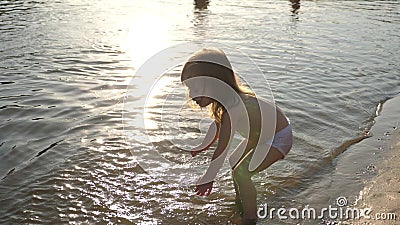 Baby splashing in the water. splashing water. Cute child happily plays on the beach. happy child bathes in the sunset on Stock Photo
