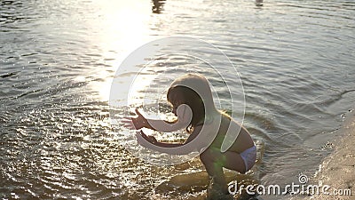 Baby splashing in the water. splashing water. Cute child happily plays on the beach. happy child bathes in the sunset on Stock Photo