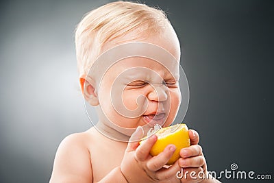 Baby squinting eyes while licking lemon Stock Photo