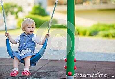 Baby swinging on swing on playground. Side view Stock Photo