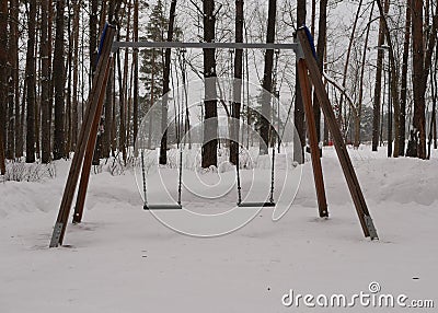 Baby swings in a snow-covered park. A deserted country park with an overcast winter day Stock Photo
