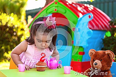 Baby toddler girl in outdoor second birthday party blowing candle on muffin Stock Photo