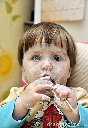 Baby tries to eat yoghurt independently Stock Photo