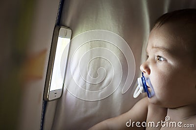 Baby watching a lullaby cartoons with mobile phone on the crib Stock Photo