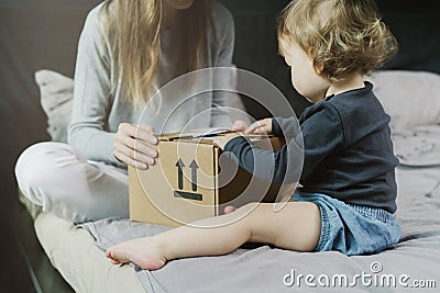 Baby and woman sitting on bed and opening a mail box with products ordered on Internet Stock Photo