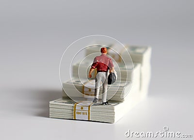 The back of a miniature man walking over a stack of cascaded bills. Stock Photo