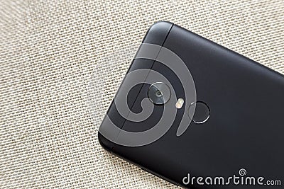 Back side of black cellphone isolated with security thumb fingerprint scanning device, camera and flash lighting on light cloth Stock Photo
