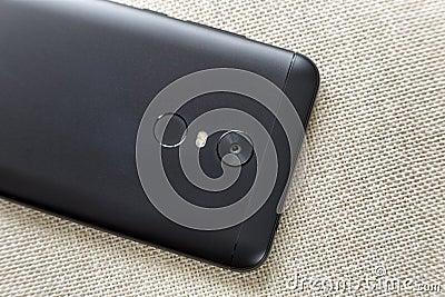 Back side of black cellphone isolated with security thumb fingerprint scanning device, camera and flash lighting on light cloth Stock Photo