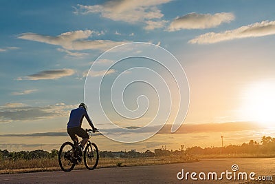 The back side of cyclist rides bicycle on sunset time background. Stock Photo