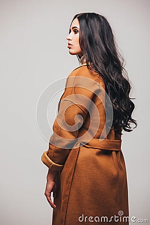 Back side of fashion studio photo of gorgeous sensual woman with dark straight hair wears elegant brown coat Stock Photo