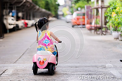 Back side of little daughter driving an electric motorcycle for toy is pink and white. Stock Photo