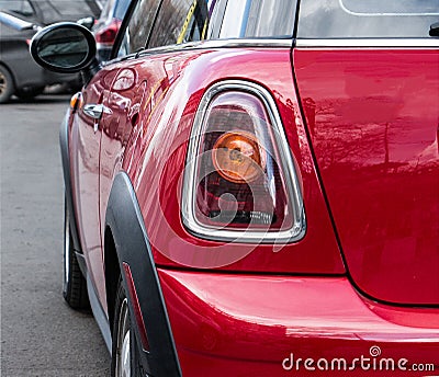 The back and side of a red Mini Cooper. One back headlight of a red Mini Cooper parked on the street. Editorial Stock Photo