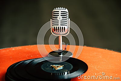 Back to 50s - nostalgic image of a 50`s microphone standing on an old orange table with old vinyl records Stock Photo