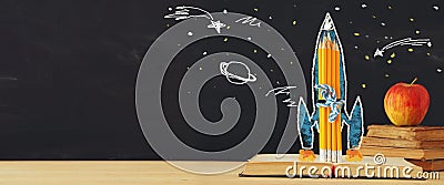 Back to school banner. rocket sketch and pencils over open book in front of classroom blackboard. Stock Photo