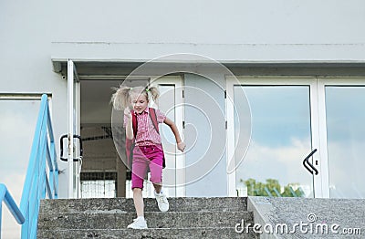 Back to school. Beautiful blond schoolgirl with red backpack running outside the primary school. Stock Photo