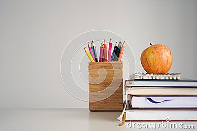 Back to school concept. Apple on books, notebook, colour pencils in stand, light gray background. Stock Photo