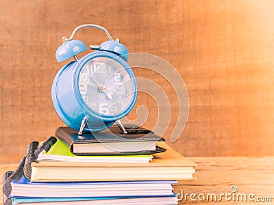 Retro style of alarm clock on stacks of books with wooden table background. Stock Photo