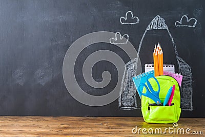 Back to school concept with small bag backpack, school supplies and rocket sketch over chalkboad background Stock Photo