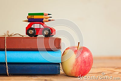 Back to school concept with stack of books and red apple and miniature car carrying colorful pencil. Stock Photo