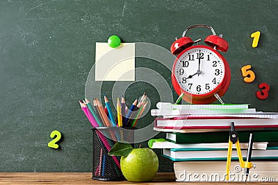 Back to school and education concept with alarm clock, green apple and stationery supplies against blackboard with numbers Stock Photo