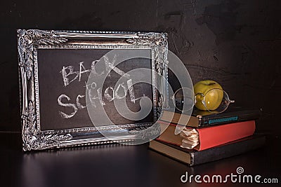 Back to school, text on chalkboard and a stack of textbooks. Textured vintage frame on a dark textured background. Stock Photo