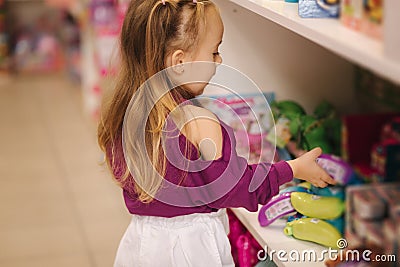 Back view of adorable little girl shopping for toys. Cute female in toy store. Happy young girl selecting toy Stock Photo